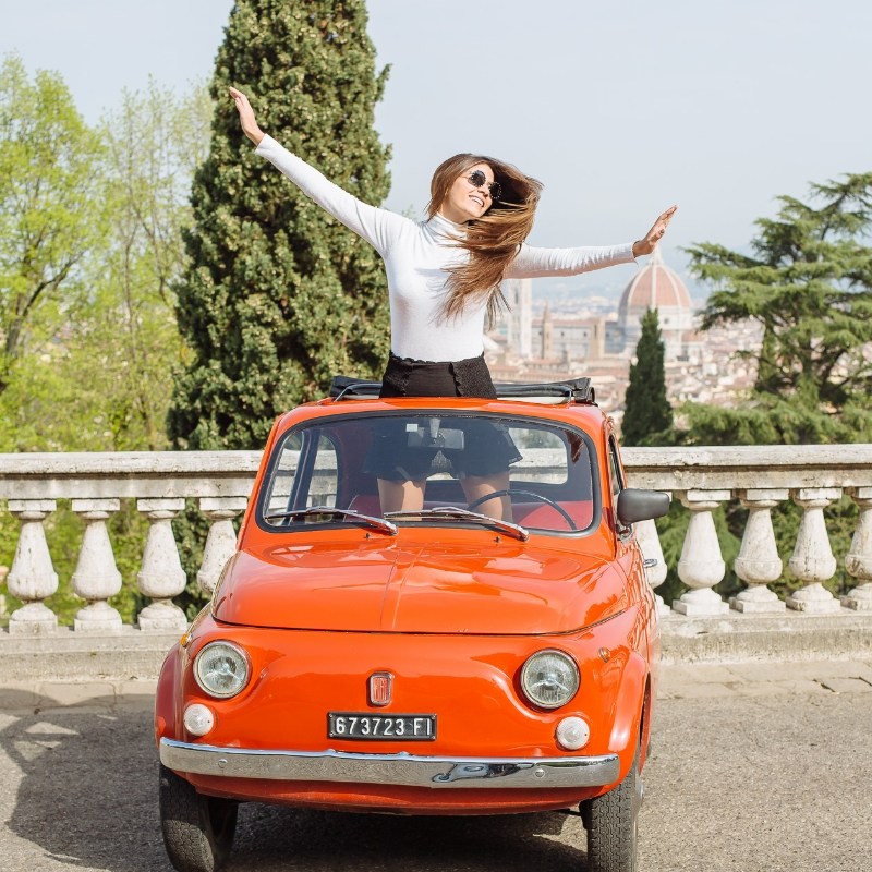 Girl sitting in red Fiat 500 in Tuscany