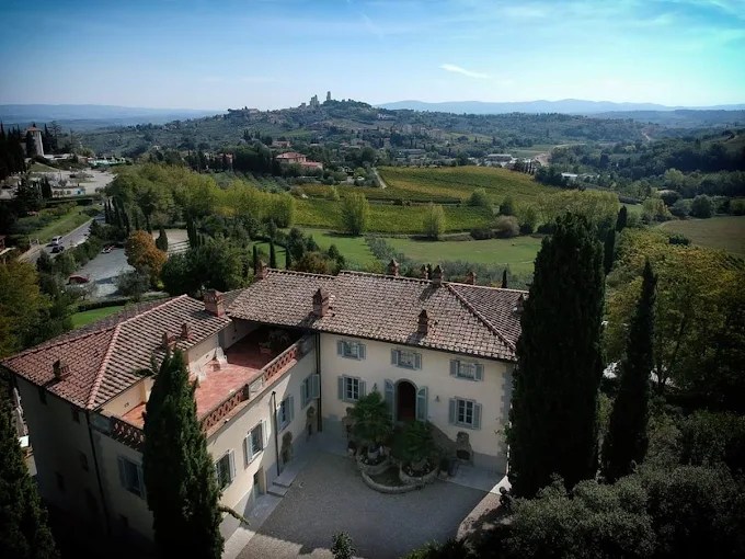 Aerial view of an Italian villa with terracotta roof, surrounded by trees and rolling hills.