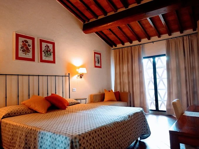 Cozy bedroom with wooden ceiling, framed art, double bed, decorative pillows, and dim lighting.