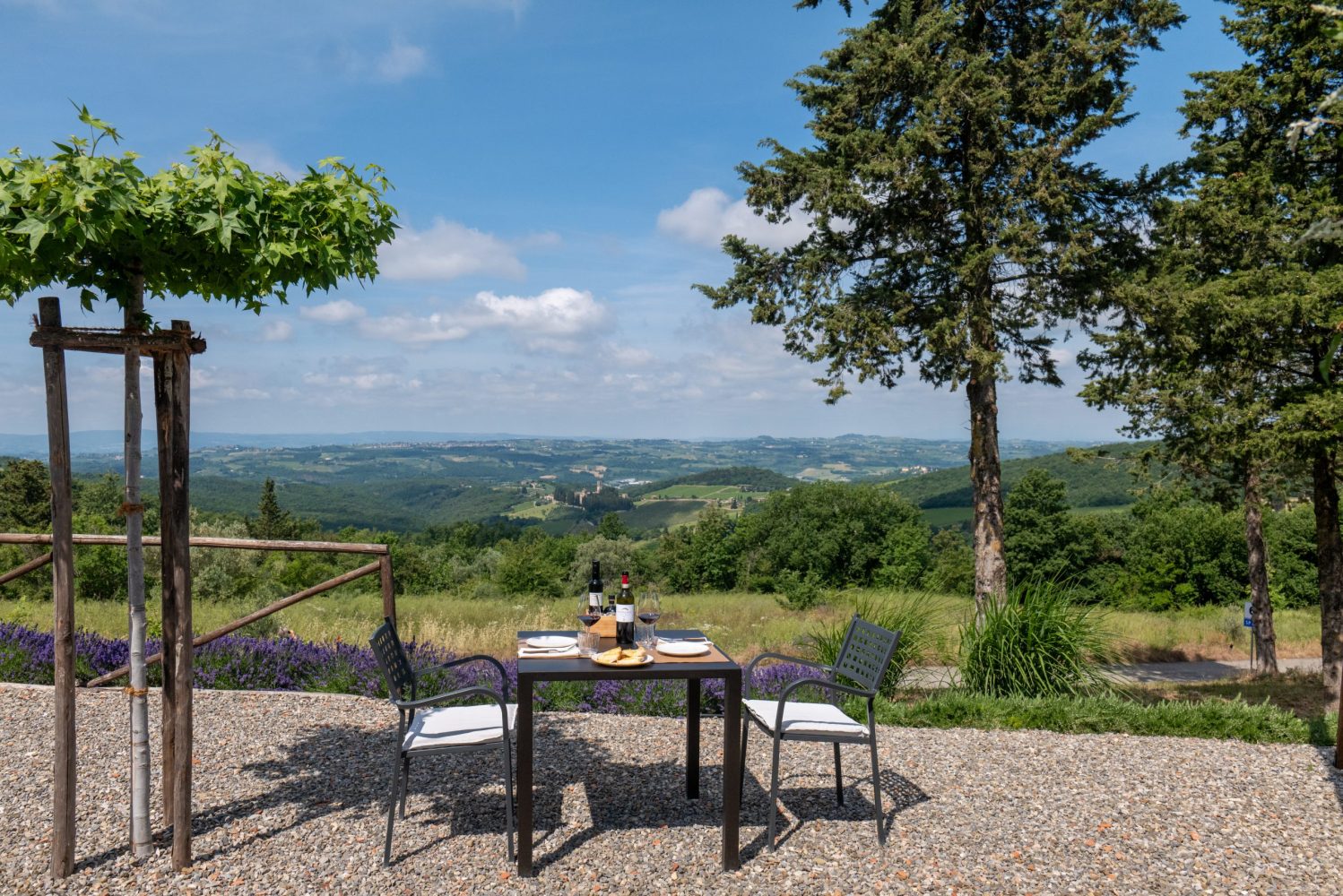 Outdoor table with two chairs overlooking a scenic hilly landscape under a clear blue sky.