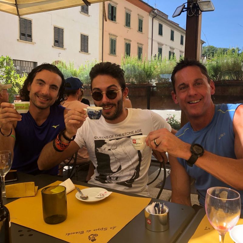 three men looking into camera drinking coffee outside in italian cafe