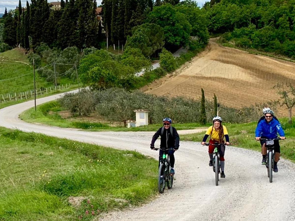 Three cyclists on a gravel road surrounded by green hills and trees.