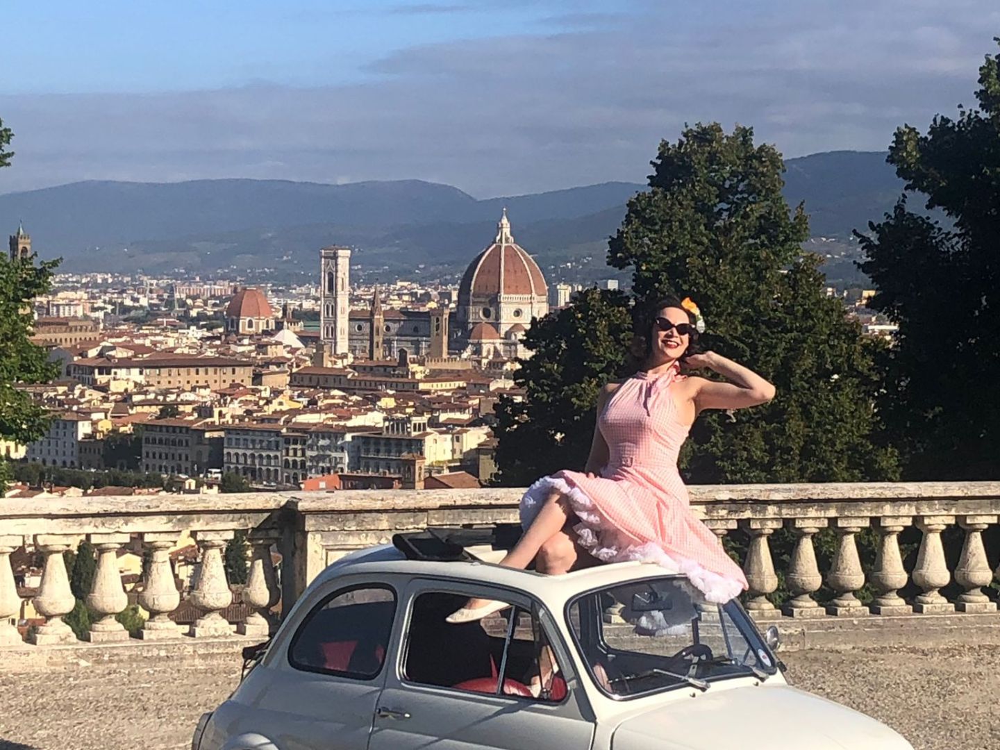 Woman in pink dress poses on vintage white car with Florence skyline in the background.
