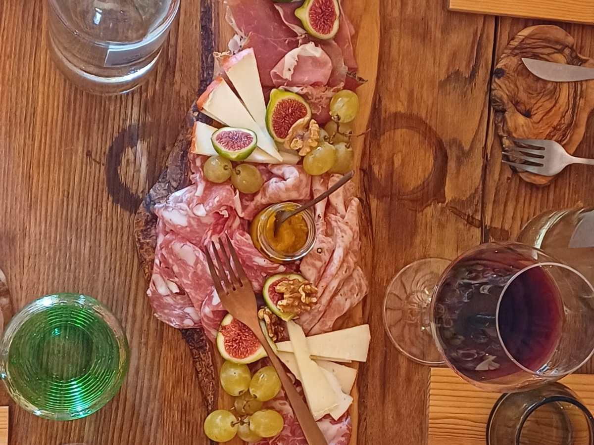 Charcuterie board with meats, cheeses, figs, grapes, and nuts on wooden table with glasses and plates.