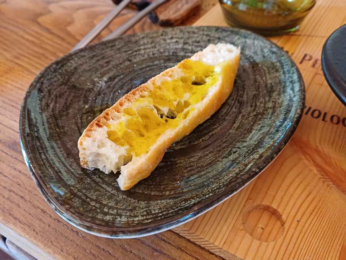 Slice of bread with olive oil on plate, wooden table setting with glasses.