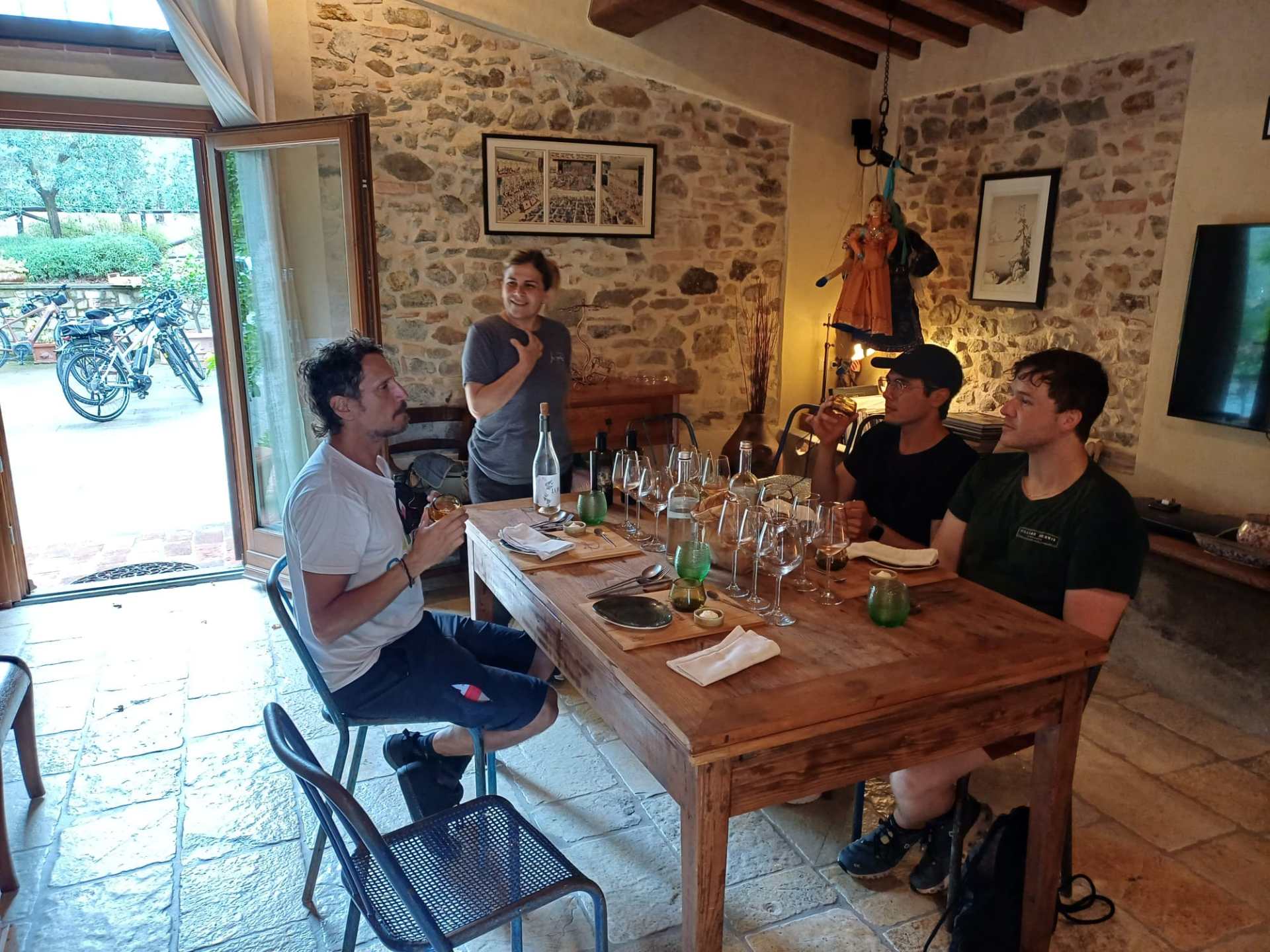 Four people sitting around a wooden table with glasses and bottles in a rustic room.