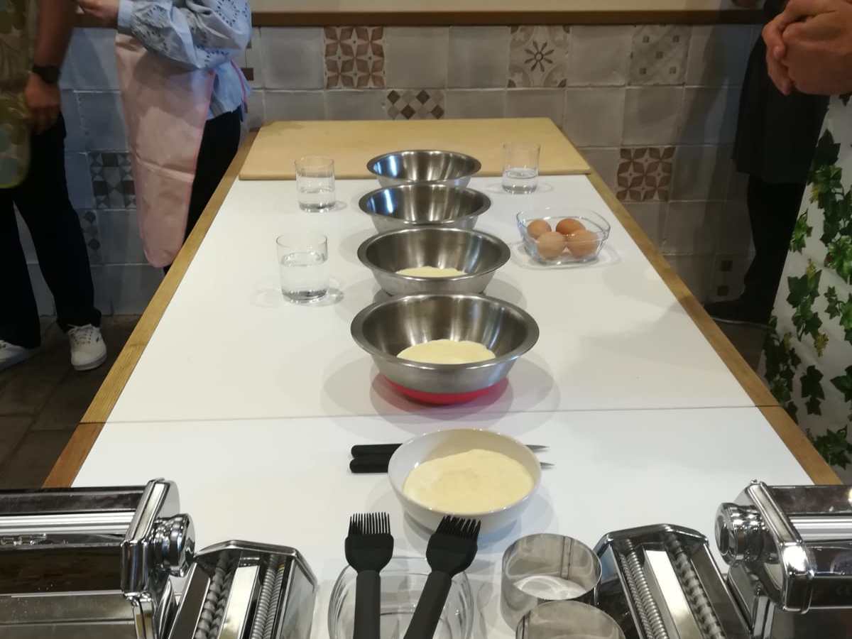 a group of people standing in a kitchen preparing pasta