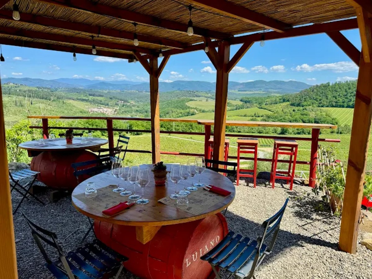 Open wooden terrace with tables overlooking a scenic vineyard and hills.