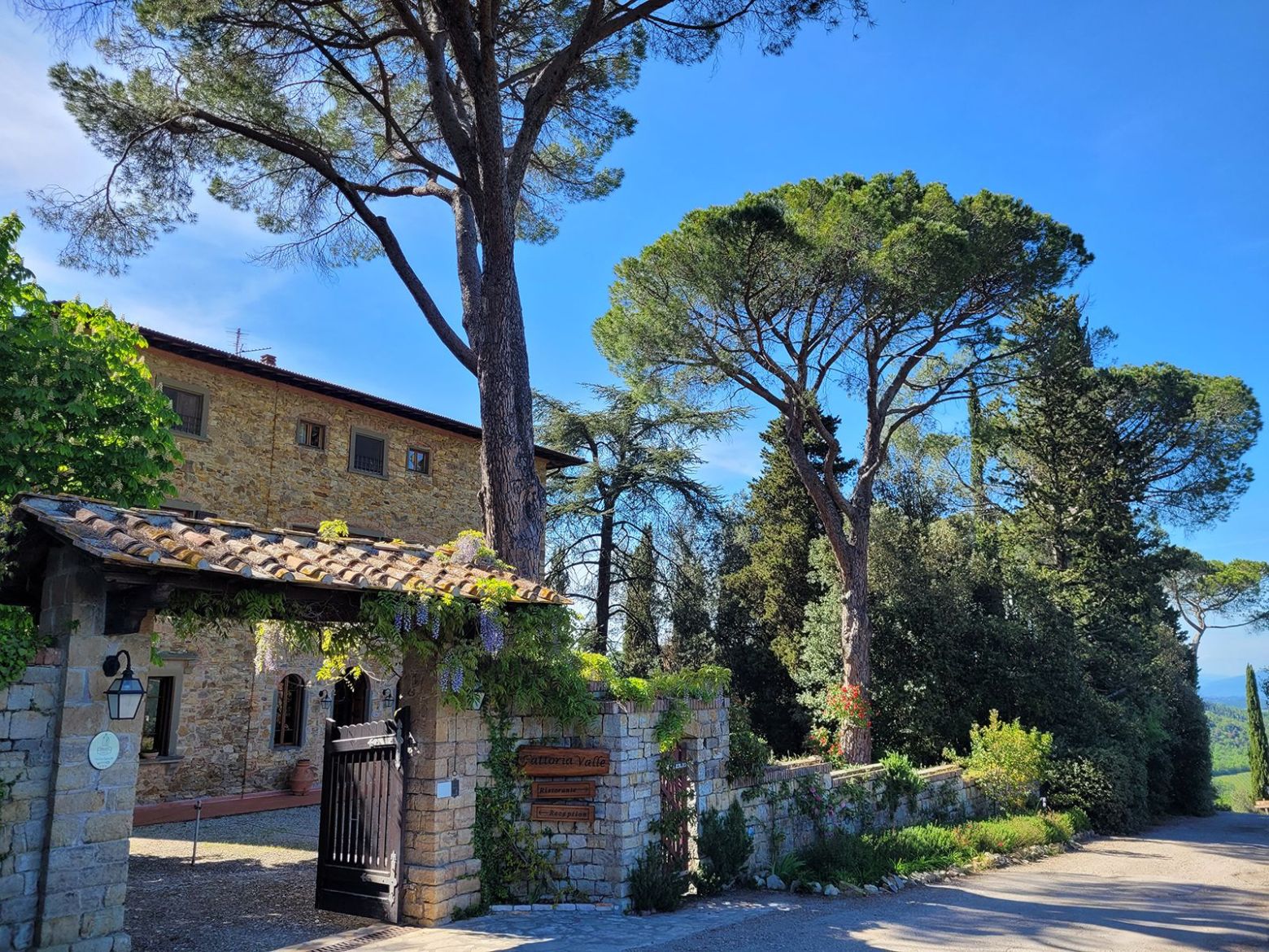 Stone building and gated entrance with tall trees under a clear blue sky.