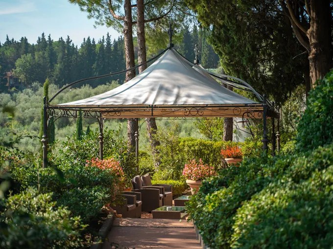 A gazebo with a white canopy surrounded by lush greenery and trees.