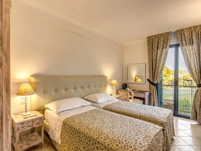 Hotel room with two twin beds, lamps, a desk, and a window with curtains.