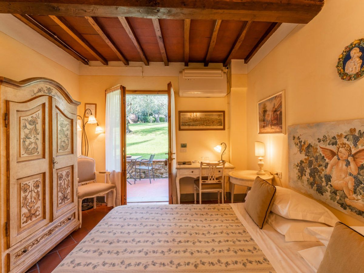 Cozy bedroom with wooden ceiling, vintage furniture, and doors open to a garden patio.