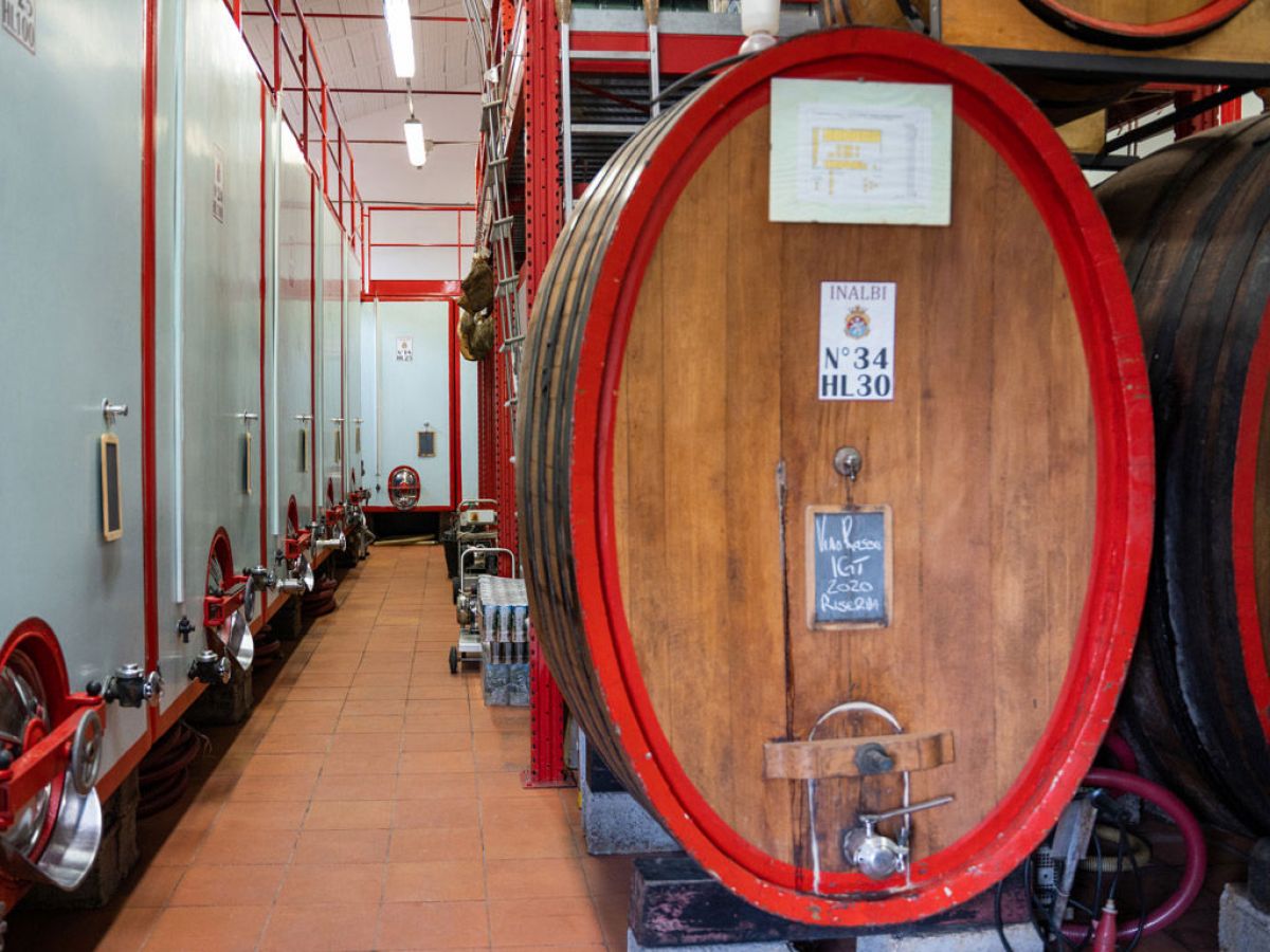 Large wooden barrels and tanks in a winery cellar with red accents and tiled floor.