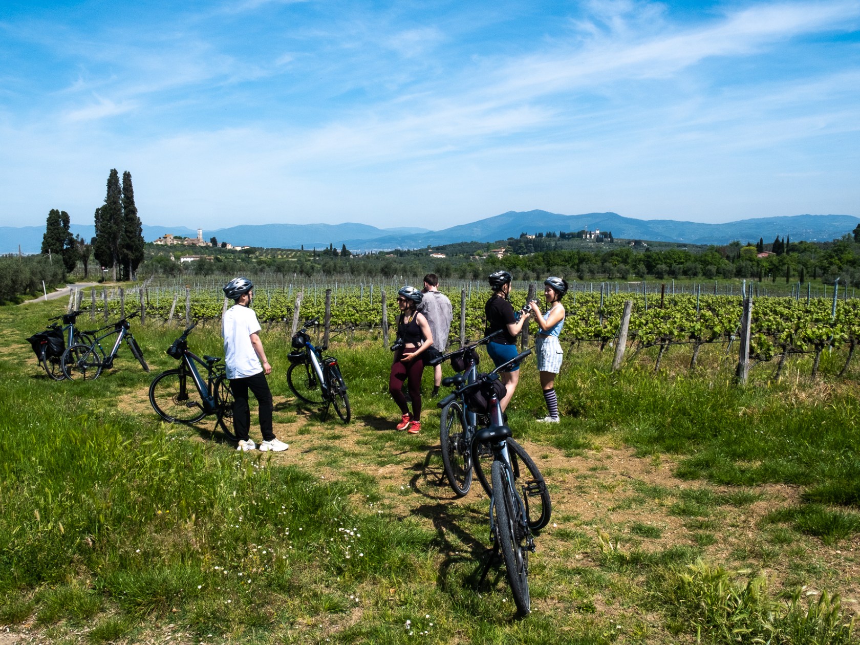 Group of cyclists resting near vineyard with scenic landscape and blue sky background.