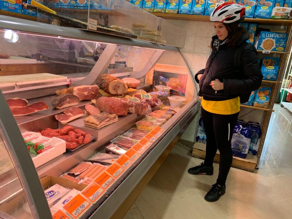 Person wearing a helmet looks at a deli counter with various meats and cheeses.