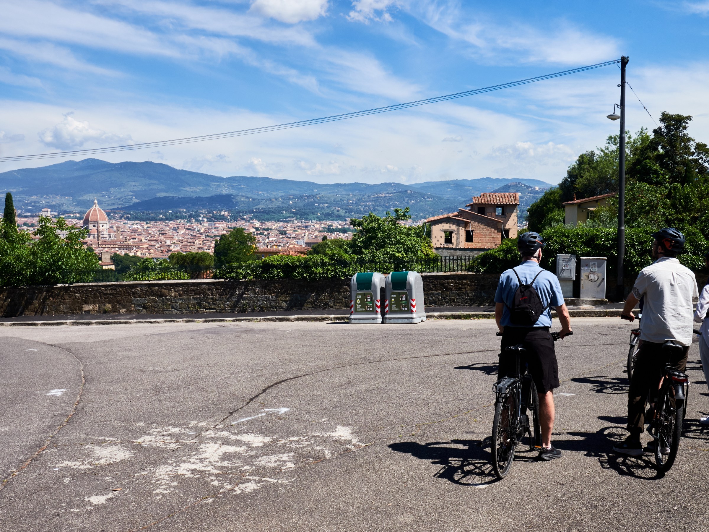 Cyclists on a road overlooking a city with dome and mountains in the background.