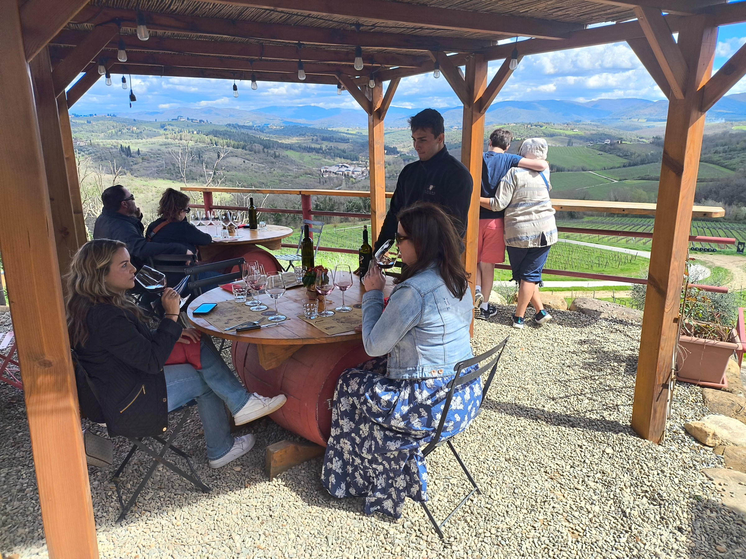 People enjoying wine at an outdoor patio with scenic hillside view.