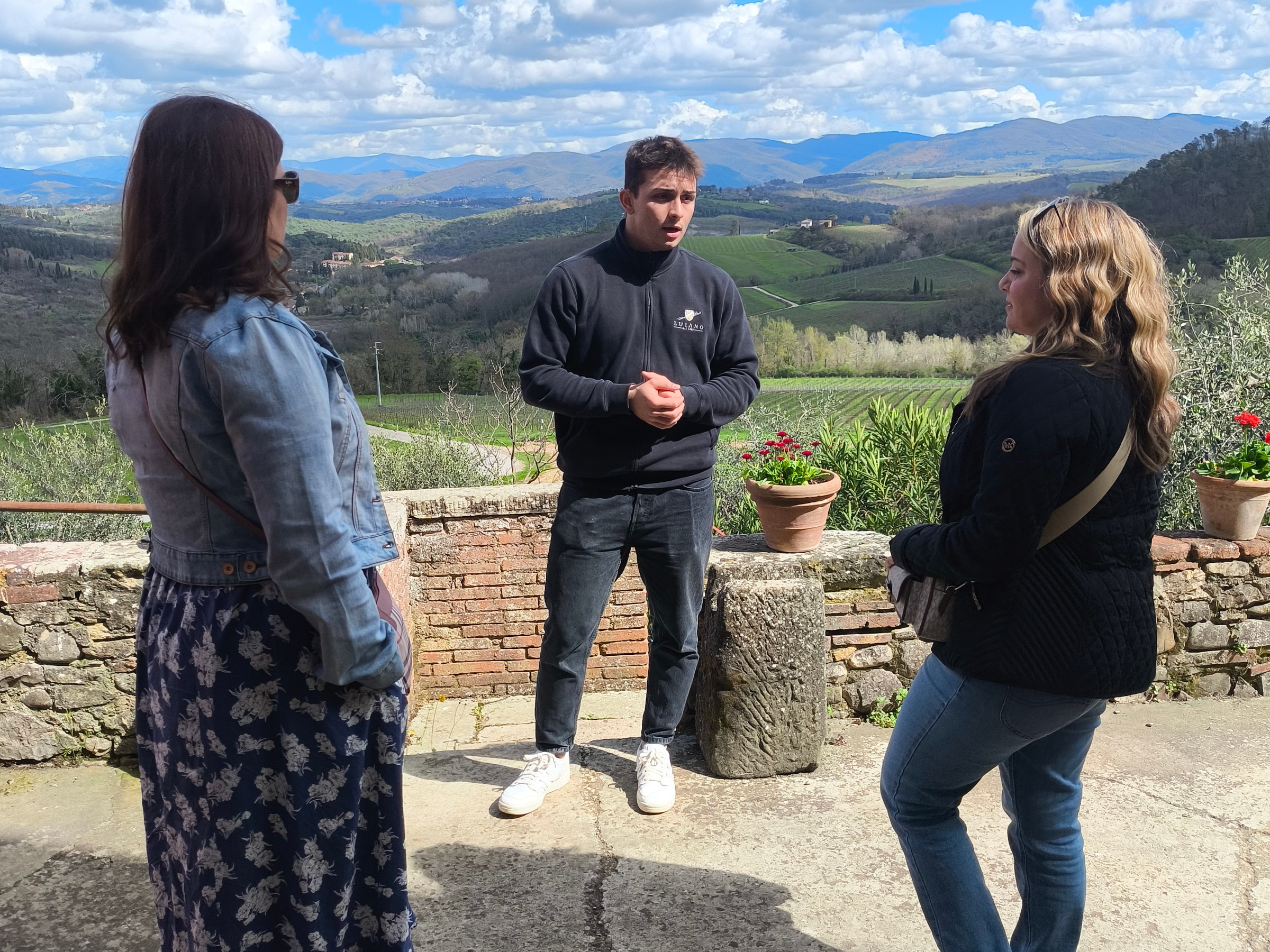 Three people standing outside with hills and clouds in the background.