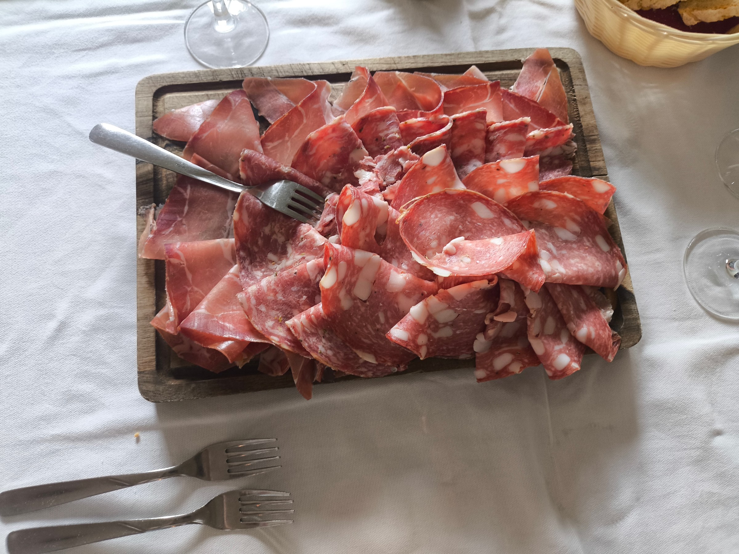 Assorted sliced meats on a tray with forks on a white tablecloth.